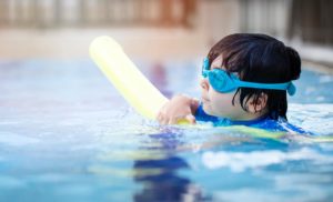 Boy with goggles swimming in a pool.